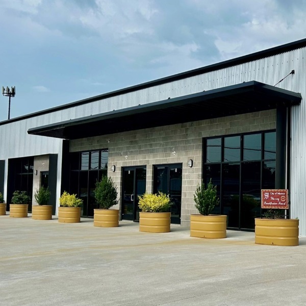 Modern commercial building with large windows and a row of yellow planters, displaying a "City of Murray Beautification Award" sign.