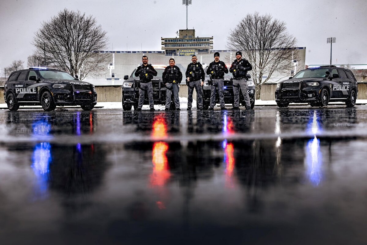 An image with an overcast sky of four police vehicles and five officers in front of a football stadium